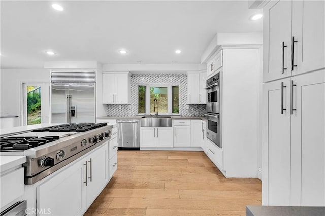 kitchen with white cabinetry, sink, light hardwood / wood-style flooring, backsplash, and appliances with stainless steel finishes