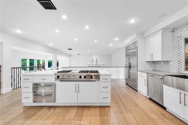 kitchen with white cabinets, tasteful backsplash, stainless steel appliances, and light hardwood / wood-style flooring