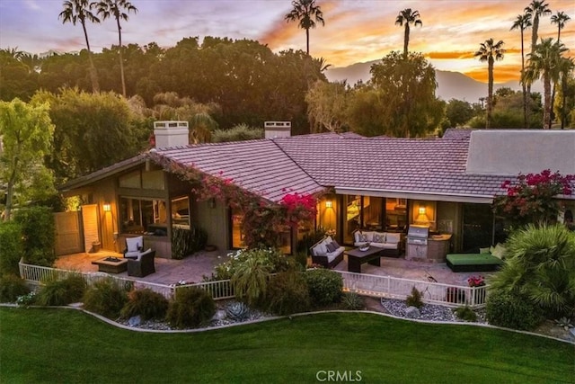 back house at dusk with a lawn, an outdoor living space, a patio area, and area for grilling