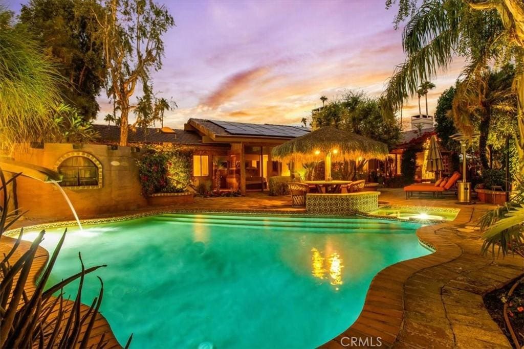 pool at dusk with pool water feature and a patio