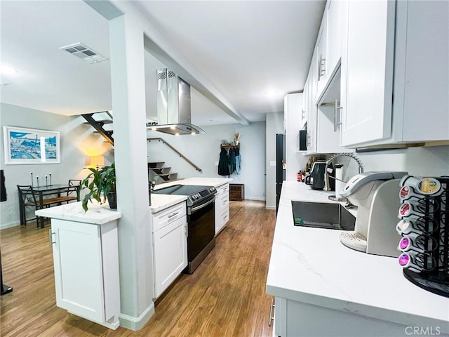 kitchen featuring black / electric stove, white cabinets, wall chimney range hood, and light wood-type flooring