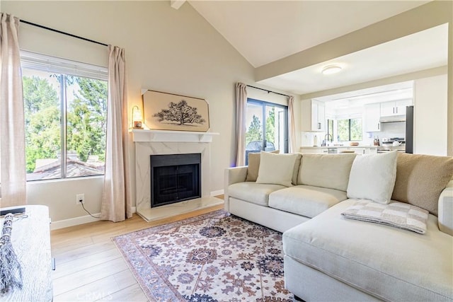 living room featuring light hardwood / wood-style floors, lofted ceiling, sink, and a high end fireplace