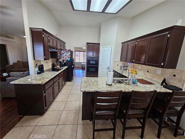 kitchen featuring light tile patterned floors, light stone counters, a peninsula, black appliances, and a sink