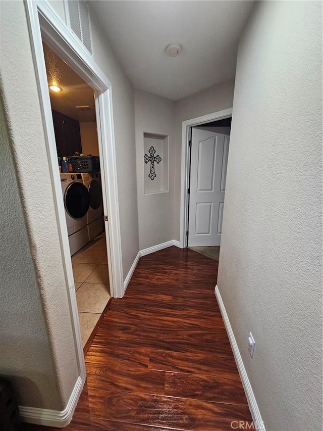 hallway featuring visible vents, a textured wall, washing machine and dryer, wood finished floors, and baseboards