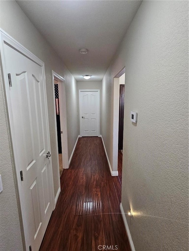 hallway featuring dark wood-style floors, a textured wall, and baseboards