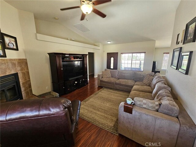 living room featuring a tile fireplace, dark hardwood / wood-style flooring, vaulted ceiling, and ceiling fan