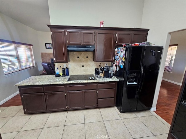 kitchen featuring backsplash, under cabinet range hood, black appliances, and light tile patterned floors