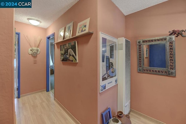 corridor with light hardwood / wood-style floors and a textured ceiling