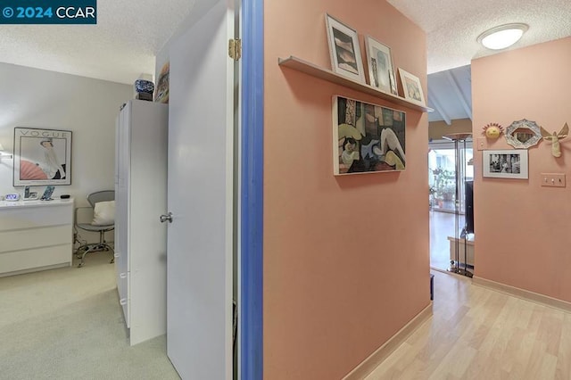 hallway featuring light wood-type flooring, beam ceiling, and a textured ceiling