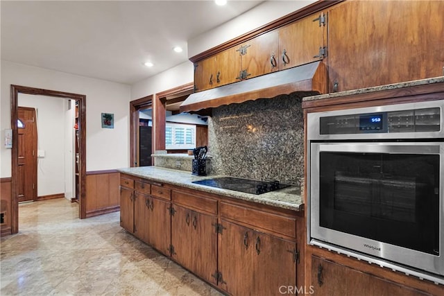 kitchen with light stone countertops, black electric cooktop, oven, and tasteful backsplash