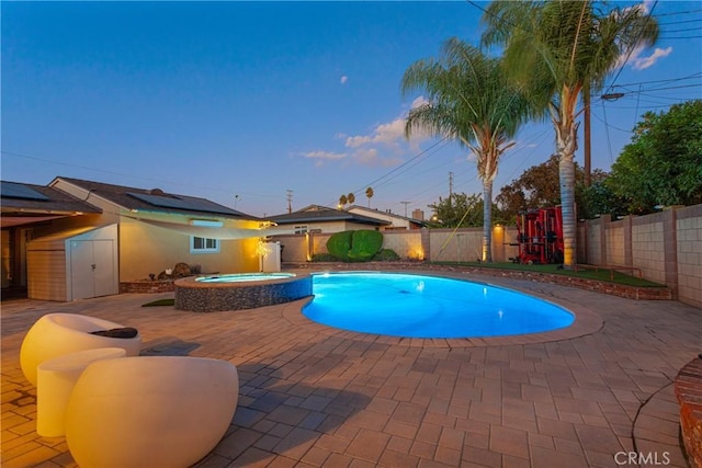 pool at dusk with an in ground hot tub and a patio