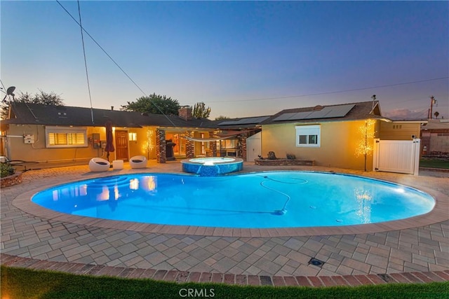 pool at dusk featuring a patio area and an in ground hot tub