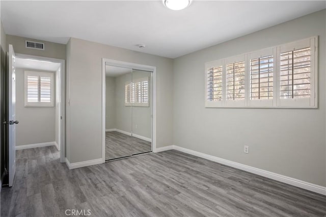 unfurnished bedroom featuring multiple windows, a closet, and hardwood / wood-style floors