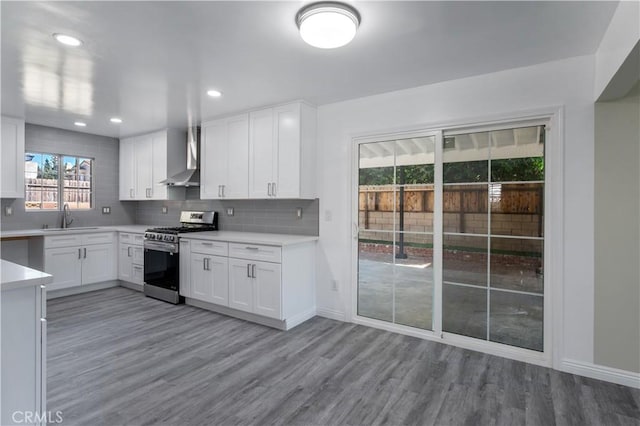 kitchen with sink, wall chimney range hood, light hardwood / wood-style floors, white cabinets, and stainless steel range with gas stovetop