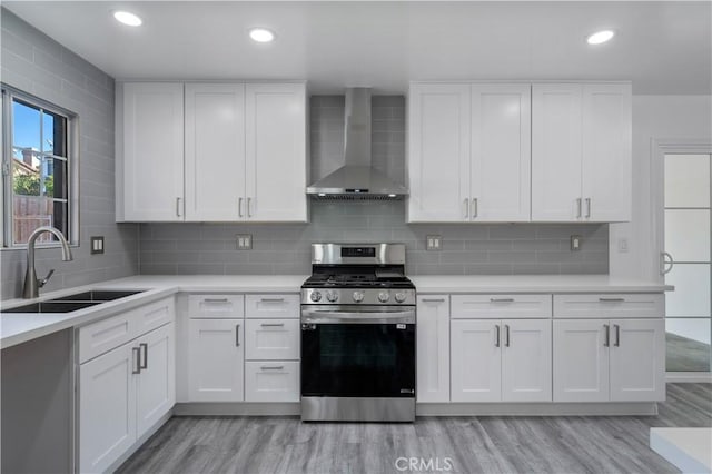 kitchen featuring white cabinets, stainless steel gas stove, sink, and wall chimney range hood