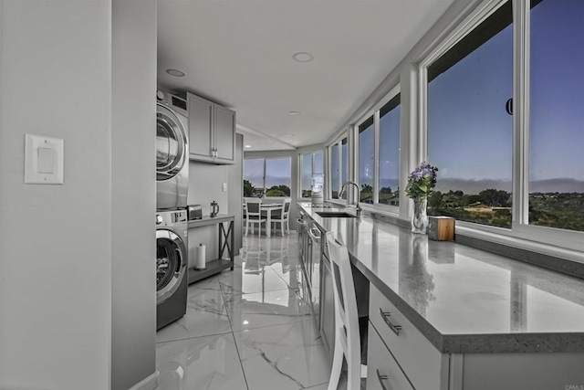 kitchen with a sink, marble finish floor, recessed lighting, and stacked washer / dryer