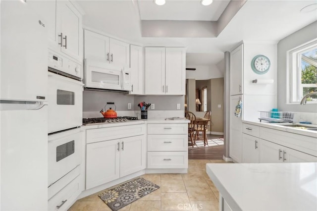 kitchen with sink, white cabinets, light tile patterned flooring, and white appliances