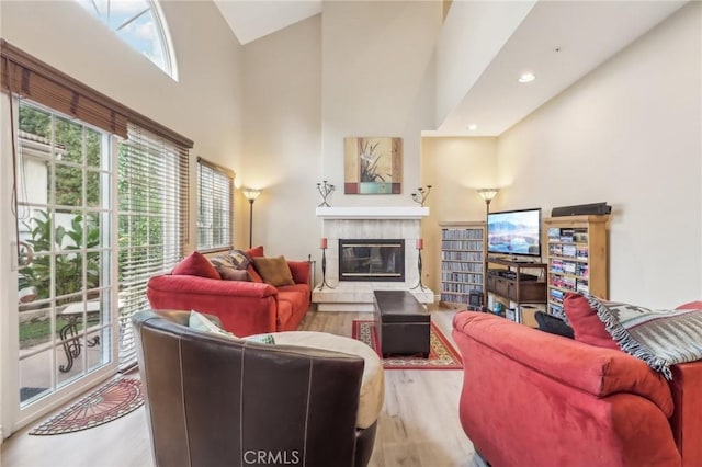 living room featuring a fireplace, light wood-type flooring, high vaulted ceiling, and a healthy amount of sunlight