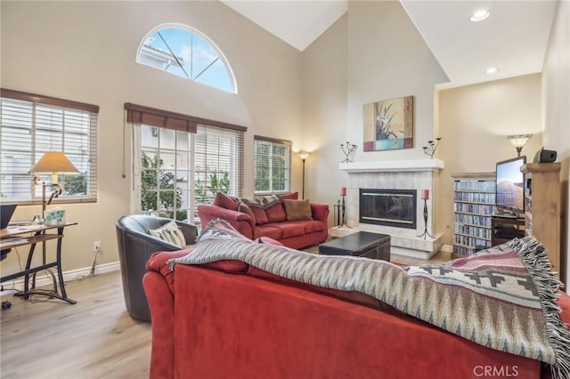 living room with a tile fireplace, light hardwood / wood-style floors, high vaulted ceiling, and plenty of natural light