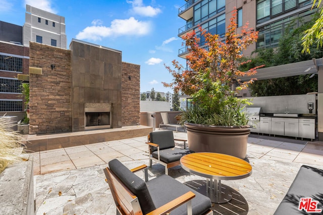 view of patio / terrace featuring area for grilling, sink, and an outdoor stone fireplace