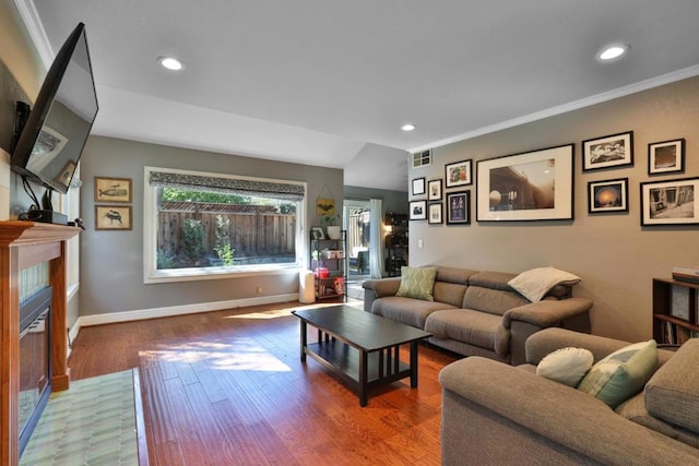 living room with a tiled fireplace, hardwood / wood-style flooring, and crown molding