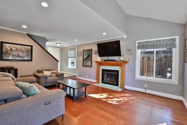 living room featuring vaulted ceiling, ornamental molding, hardwood / wood-style floors, and a tile fireplace