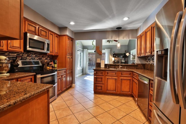 kitchen featuring light tile patterned floors, sink, appliances with stainless steel finishes, hanging light fixtures, and dark stone counters