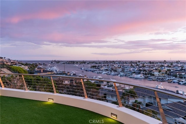 balcony at dusk featuring a water view