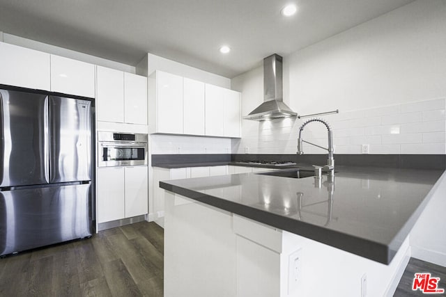 kitchen featuring white cabinets, wall chimney range hood, kitchen peninsula, and appliances with stainless steel finishes