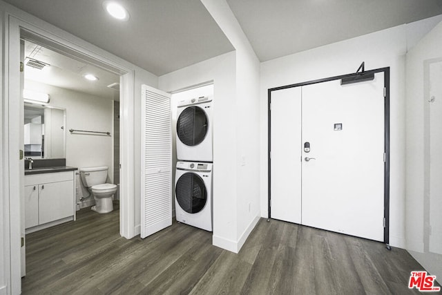 laundry room with stacked washer and dryer, dark wood-type flooring, and sink