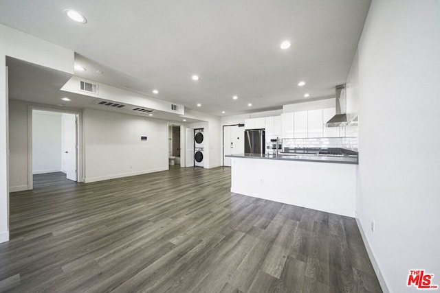 kitchen featuring stainless steel refrigerator, wall chimney exhaust hood, dark wood-type flooring, white cabinets, and stacked washer and clothes dryer