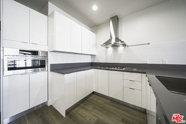 kitchen featuring white cabinets, wall chimney exhaust hood, dark wood-type flooring, and appliances with stainless steel finishes