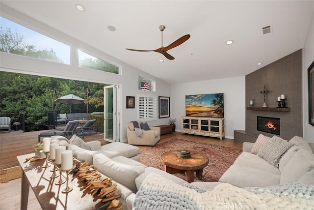 living room with ceiling fan, a fireplace, high vaulted ceiling, and light hardwood / wood-style flooring