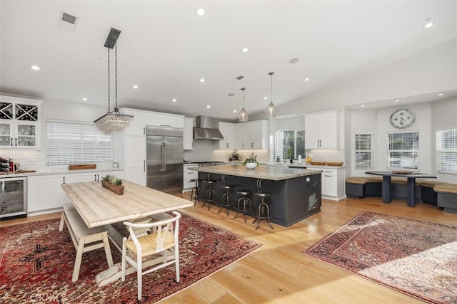 kitchen featuring a center island, white cabinets, wall chimney range hood, hanging light fixtures, and appliances with stainless steel finishes