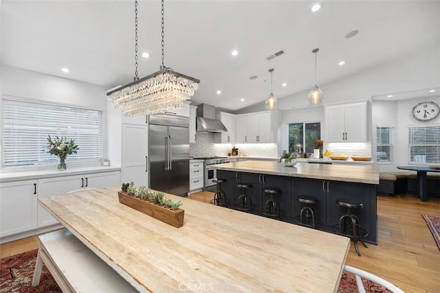 kitchen featuring pendant lighting, a center island, high end appliances, white cabinets, and wall chimney range hood