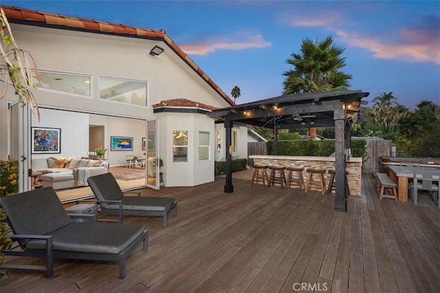 deck at dusk featuring exterior bar and an outdoor living space