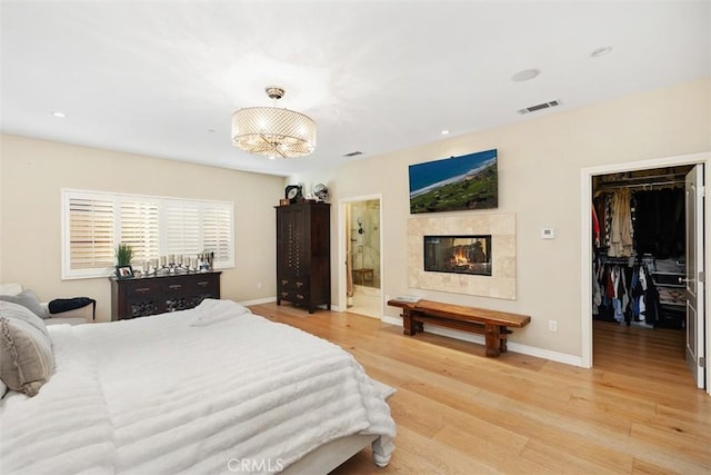 bedroom featuring a spacious closet, an inviting chandelier, light hardwood / wood-style flooring, ensuite bathroom, and a closet