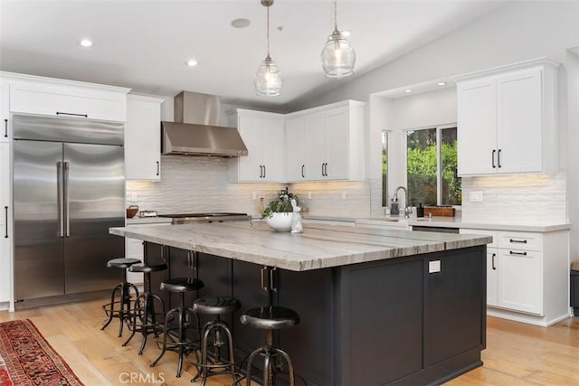 2308 S Ola Vis, San Clemente, CA 92672 - kitchen with wall chimney range hood, light stone counters, built in fridge, a center island, and white cabinetry