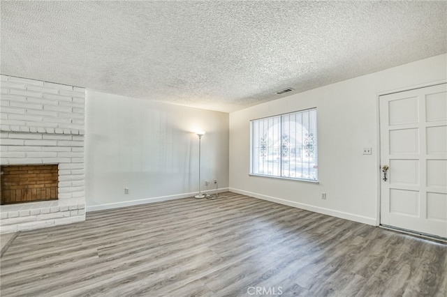 unfurnished living room with a textured ceiling, light wood-type flooring, and a brick fireplace