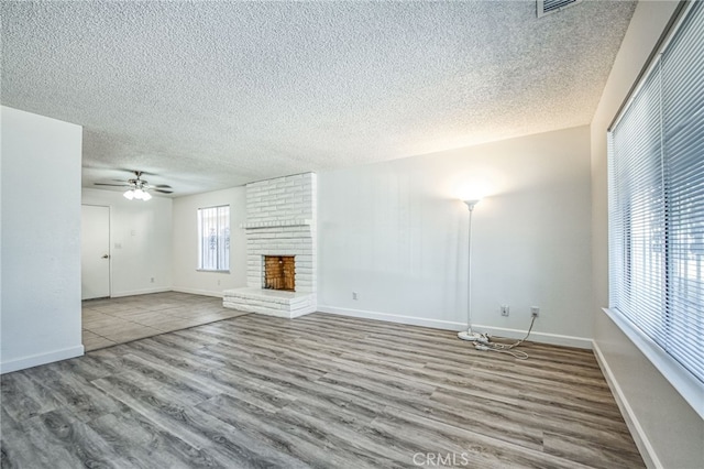 unfurnished living room with wood-type flooring, a textured ceiling, a brick fireplace, and ceiling fan