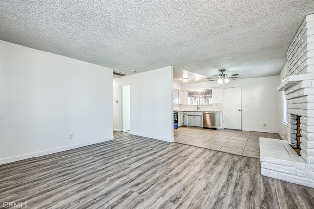 unfurnished living room featuring ceiling fan, light hardwood / wood-style flooring, a textured ceiling, and a brick fireplace