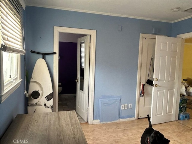 bedroom with ensuite bathroom, light hardwood / wood-style floors, and ornamental molding