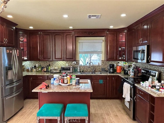 kitchen with light wood-type flooring, appliances with stainless steel finishes, a center island, and sink