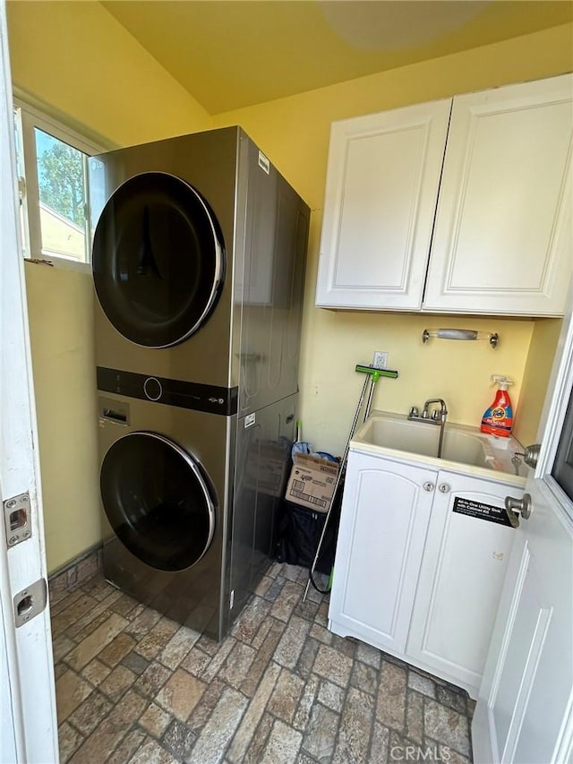 washroom with cabinets, stacked washer / dryer, and sink