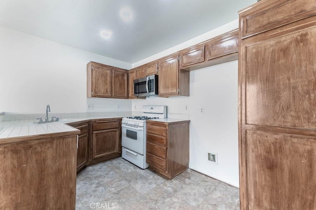 kitchen with white range with gas stovetop, sink, and tile countertops