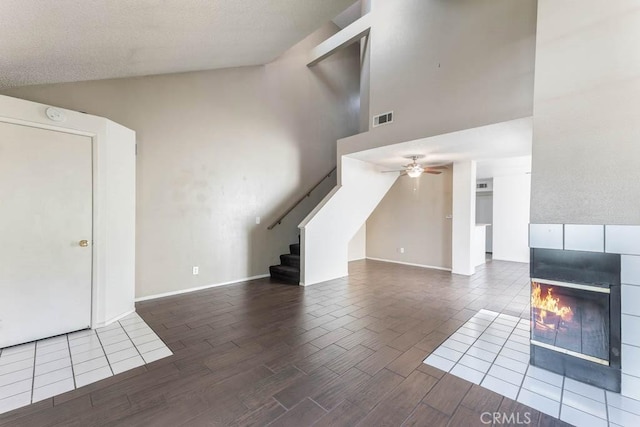 unfurnished living room with ceiling fan, high vaulted ceiling, and a tiled fireplace