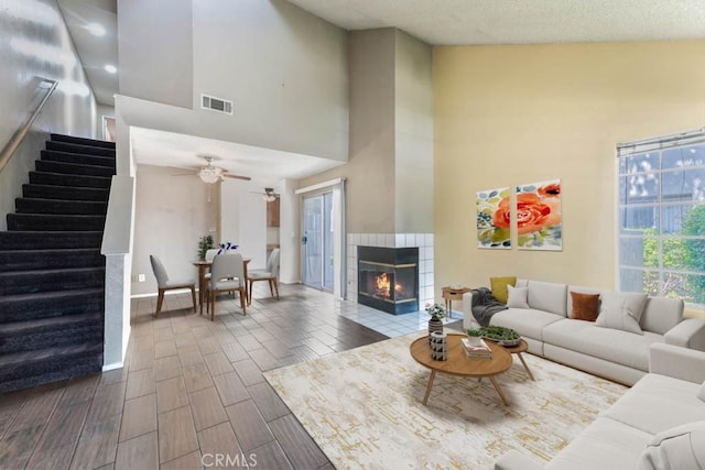 living room with ceiling fan, a tiled fireplace, and a towering ceiling