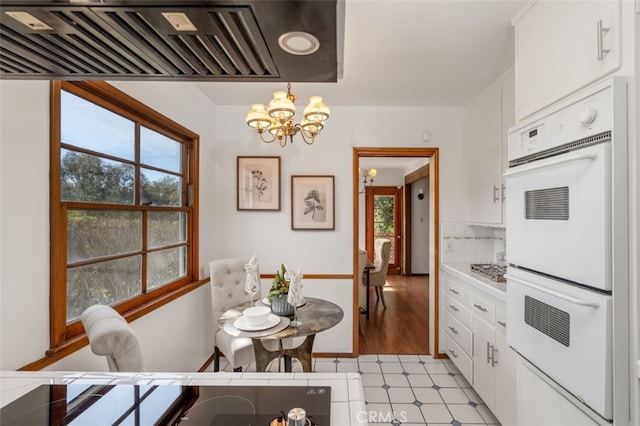 kitchen with light wood-type flooring, white double oven, a chandelier, white cabinetry, and hanging light fixtures