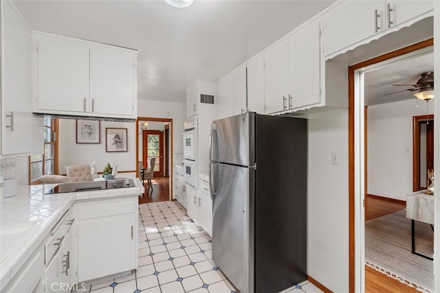 kitchen with tile countertops, stainless steel fridge, white cabinets, and light wood-type flooring