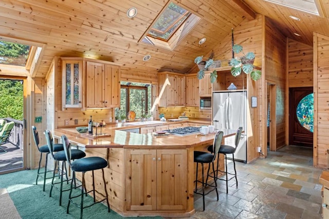 kitchen with high vaulted ceiling, a skylight, stainless steel appliances, and wood walls